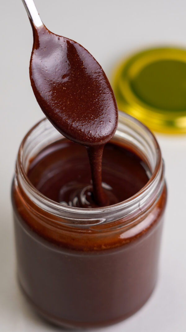 Close-up of 3 ingredient healthy Nutella in a glass jar with a spoon dipping in the chocolate hazelnut spread