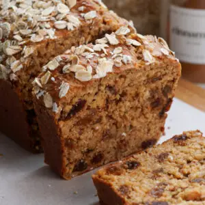 Sweet cottage cheese bread with raisins, sliced on a wooden board with parchment paper and oats sprinkled on top.