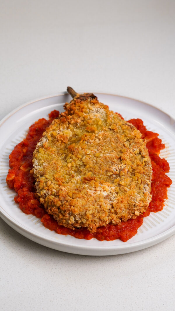 Crispy aubergine fillet coated in golden panko breadcrumbs on a plate with tomato sauce