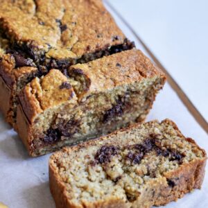 Healthy banana bread with two slices on a chopping board lined with parchment paper