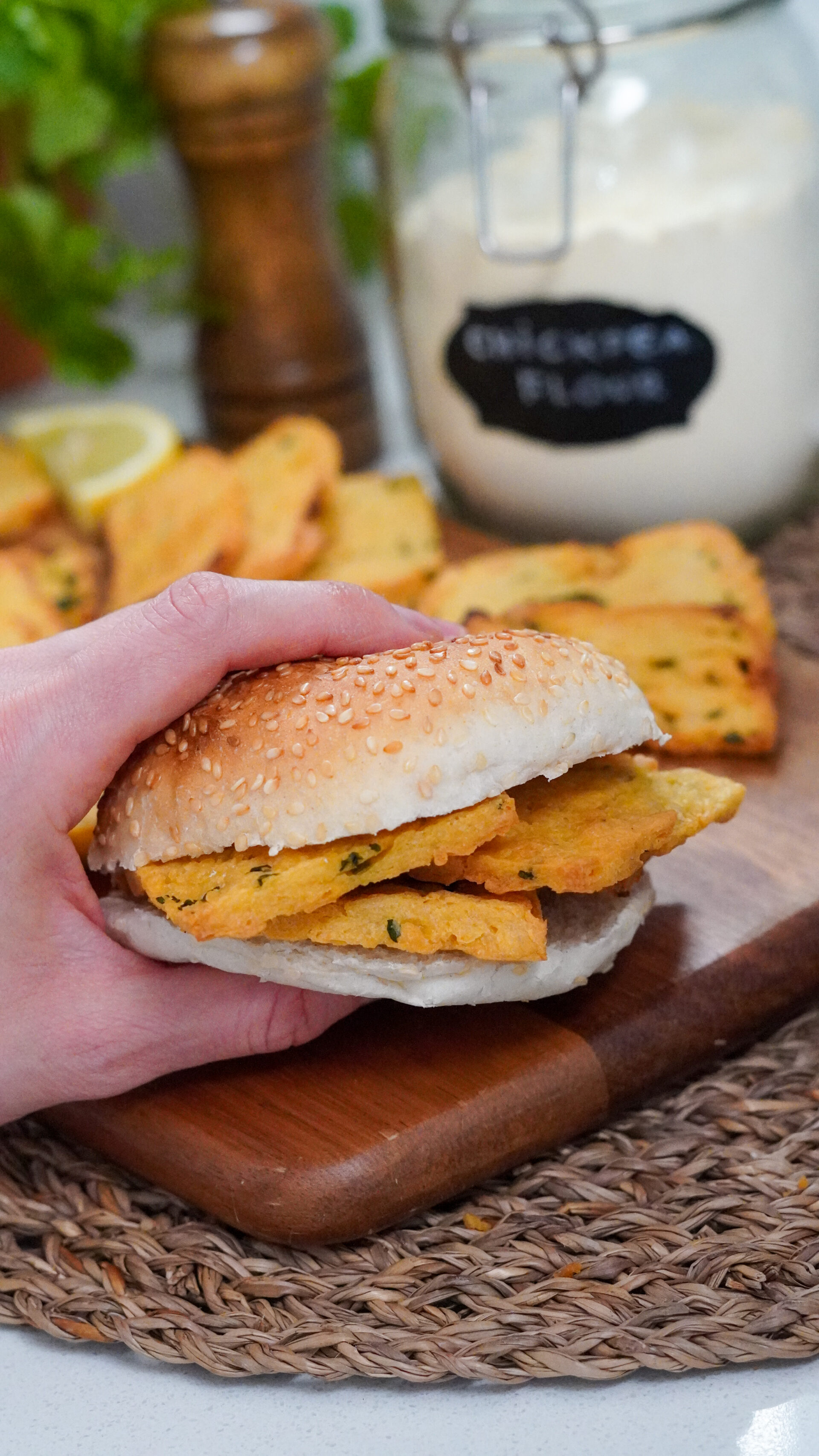 Hand holding a Sicilian panelle sandwich in a burger bun, with more panelle in soft focus in the background.