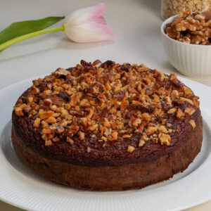Whole blender date and walnut cake topped with walnuts on a white plate