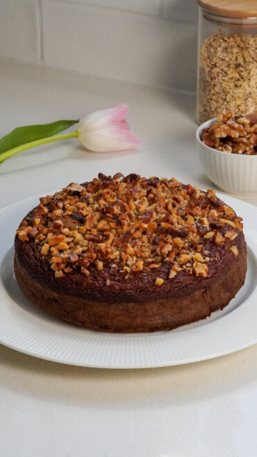 Whole blender date and walnut cake topped with walnuts on a white plate