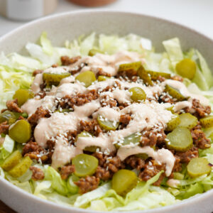 Big Mac Salad served in a bowl with lettuce, cheesy beef mince, sliced pickles, and yoghurt burger sauce, sprinkled with sesame seeds – a low-carb, high-protein meal.