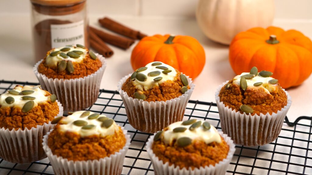 Healthy pumpkin cream cheese muffins with creamy maple filling and pumpkin seeds on top, on a cooling rack.