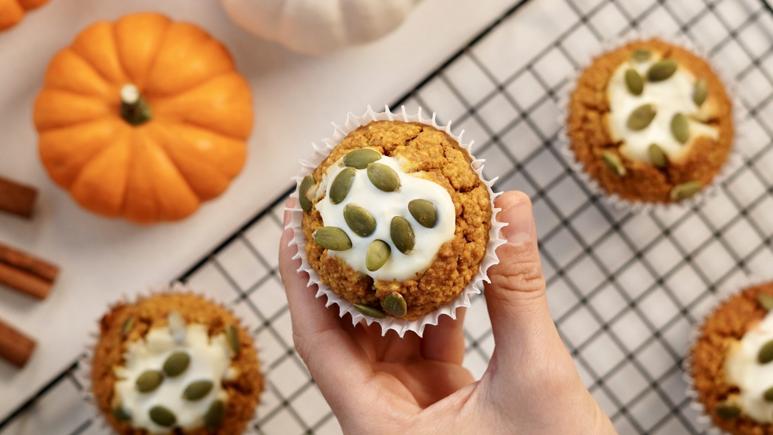 hand holding a pumpkin muffin with cream cheese topping